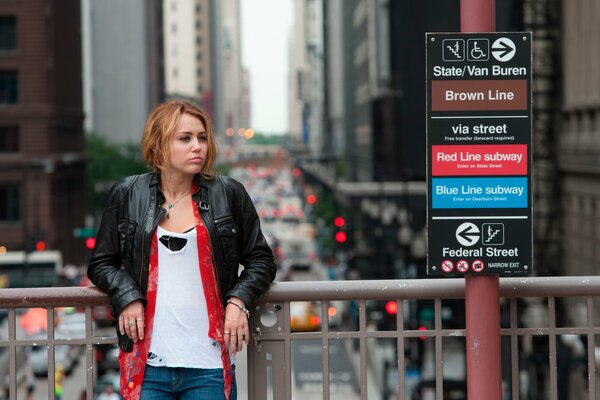 Una chica con una chaqueta de cuero está de pie en un puente