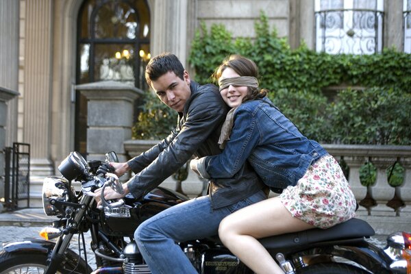 A guy takes a girl with his eyes closed on a motorcycle