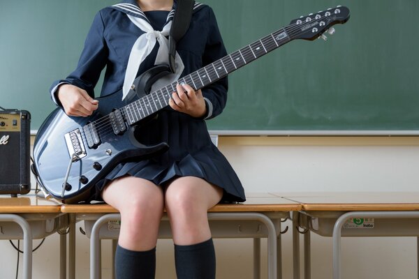 Las piernas de una chica sentada en una mesa con una guitarra en la mano