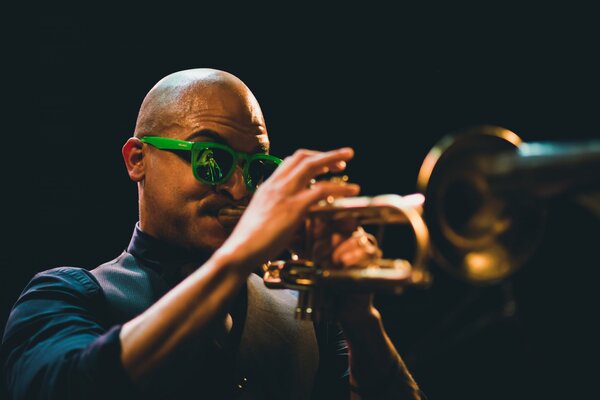 A musician in green glasses plays the trumpet in the night light