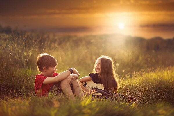 Ein Junge und ein Mädchen sitzen im Gras und lachen und Deaochka spielt Gitarre