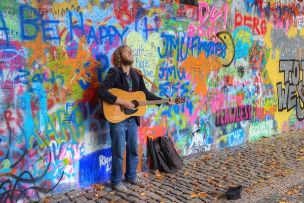 Muzyk gra na gitarze stojąc pod ścianą