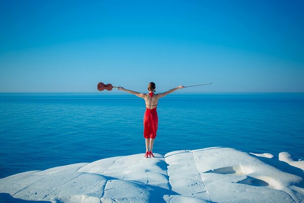 Una chica con un vestido rojo con un violín en el fondo del mar