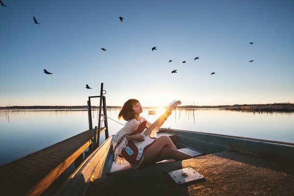 A girl with a guitar sitting on the shore of a lake