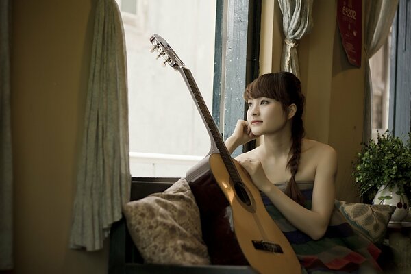 Fille assise avec une guitare près de la fenêtre