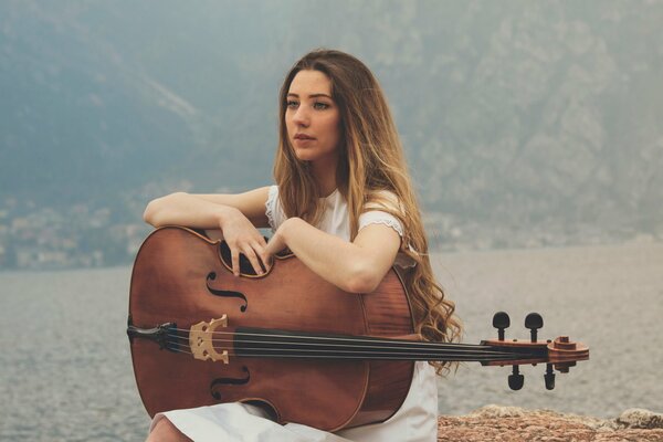 Fille assise au bord du lac avec violoncelle sur ses genoux