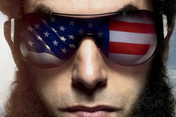 The face of a man with glasses with a US flag