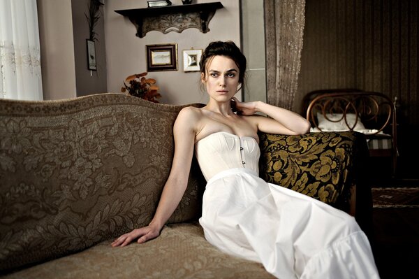 Keira Knightley en robe blanche stdit sur le canapé