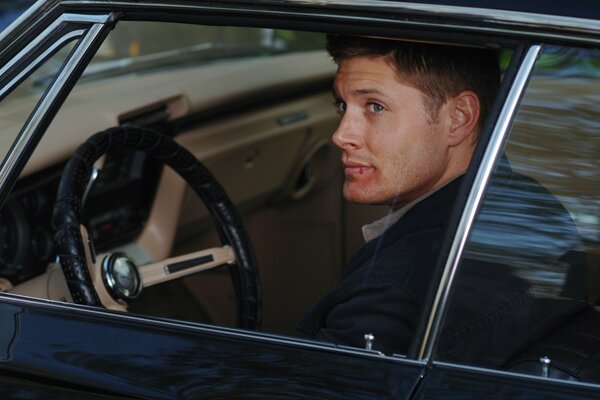 Dean Winchester from Supernatural is sitting behind the wheel of his favorite car