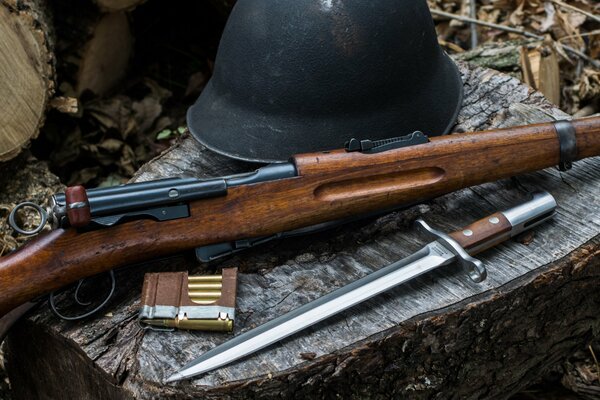 There is a set of weapons on the stump. Bayonet-knife, rifle, helmet