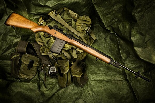 A semi-automatic rifle is lying on a green backpack