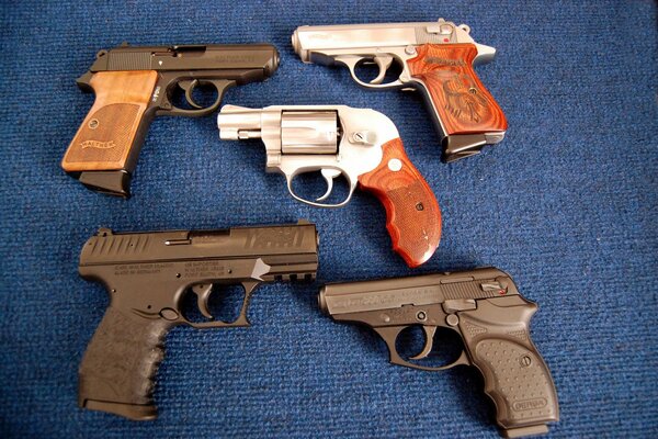 Five pistols are lying on a blue background