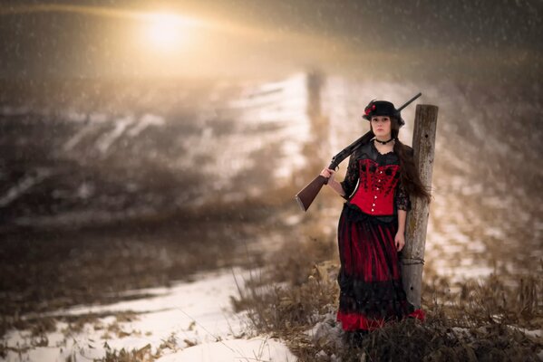 A woman with a gun in her hand stands among the snow and grass