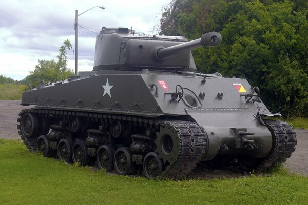 Tank of the World War II period on the green grass next to the trees against the sky