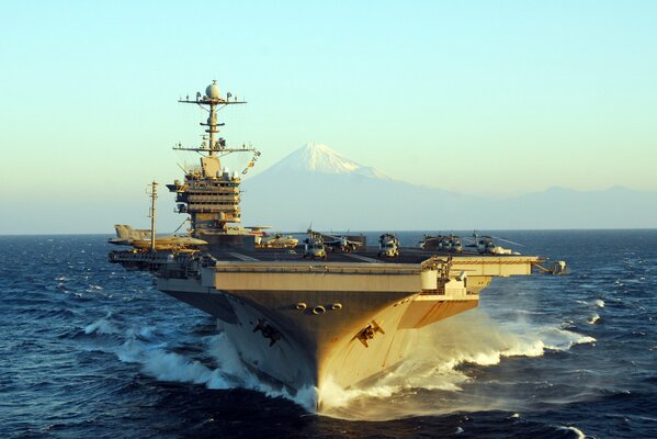 Aircraft carrier of the type Nimitz dissects waves on the background of a mountain peak