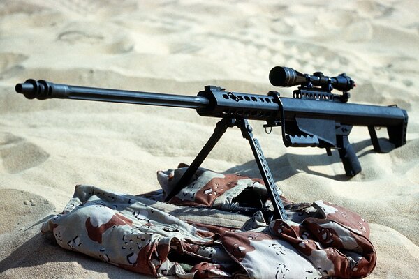 The rifle is on camouflage in the sand