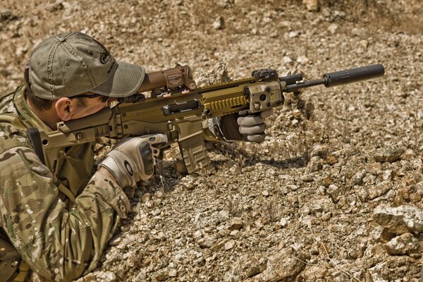 A sniper takes aim with a rifle against a background of stones