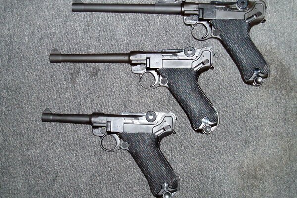 Three Luger pistols on a gray background