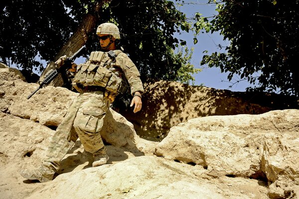 A soldier with a machine gun goes down the rocks