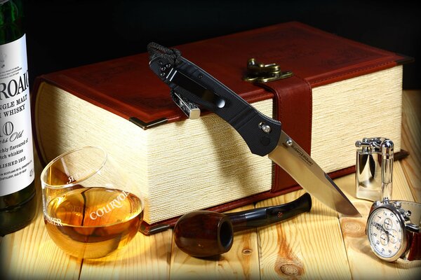 Das Messer liegt auf einem dicken Buch und daneben steht ein Whisky mit einer Tube