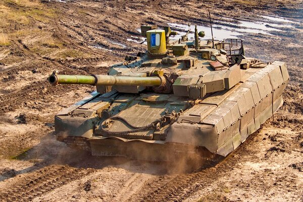 A powerful armored tank is rolling through the field and mud