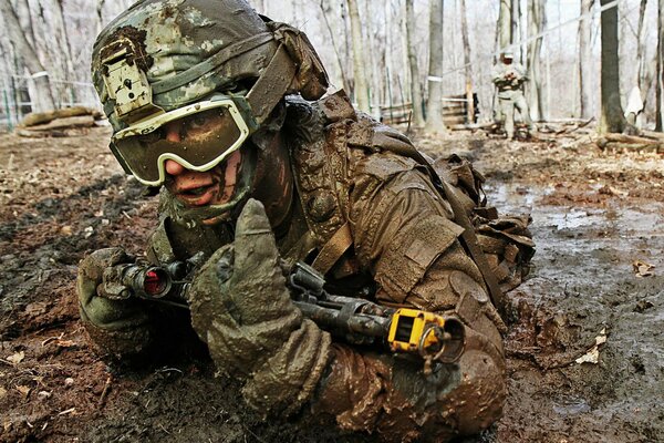 Soldat avec des armes et en uniforme est en train de s entraîner, rampant sur le sol boueux après la pluie