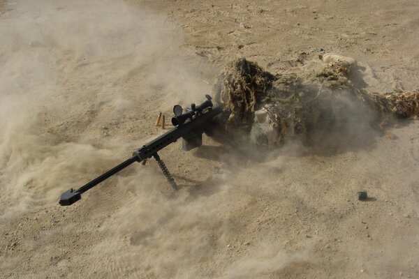 A sniper in a camouflage net merged with the sand