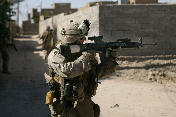 A US soldier takes aim with an m4 weapon, against a stone wall