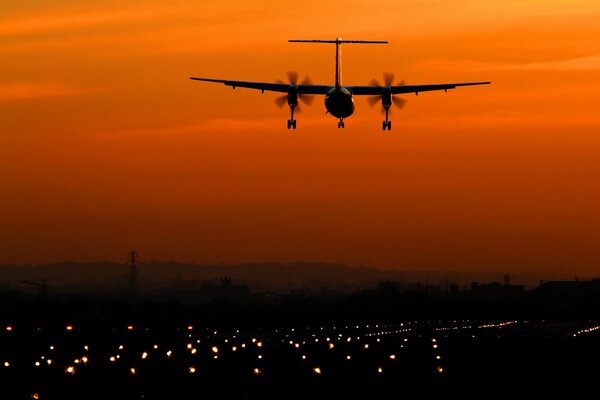 Avión en el fondo del cielo amarillo de la puesta del sol, las luces de la ciudad de la noche