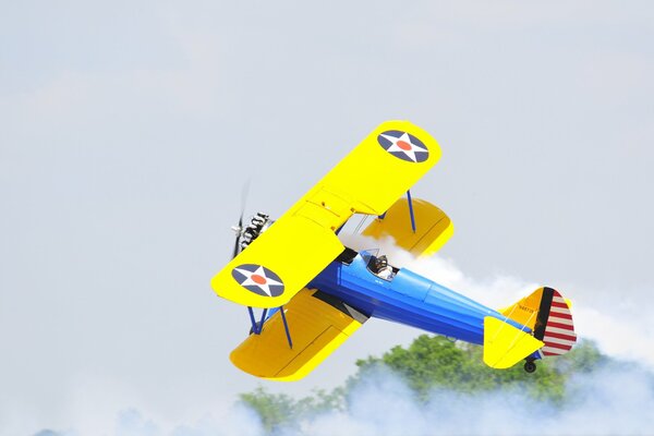 Ein gelb-blauer Doppeldecker fliegt im Nebel