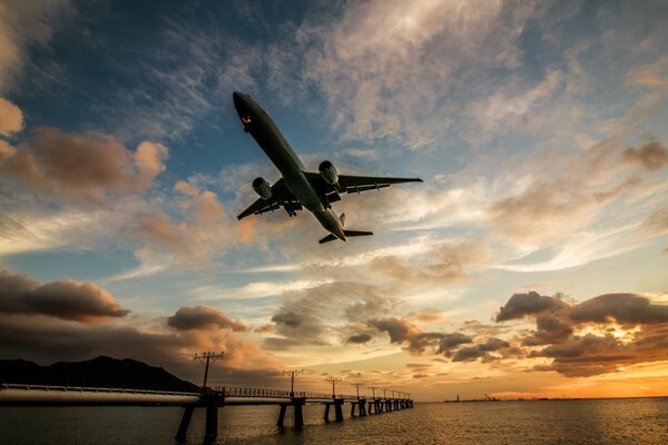 Avión bajo sobre el río y el puente al atardecer