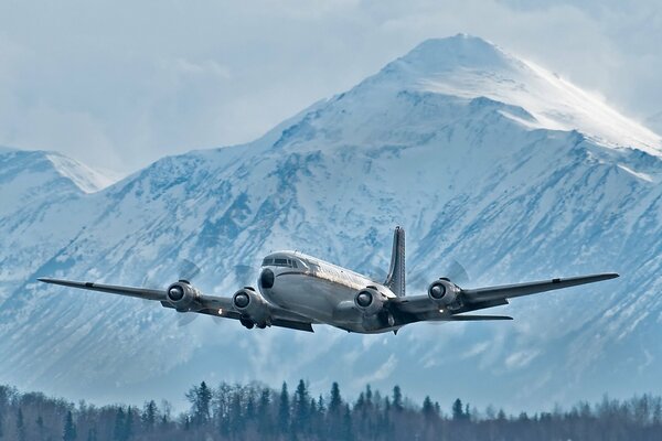 Военно-транспортный самолёт в небе на фоне заснеженной горы