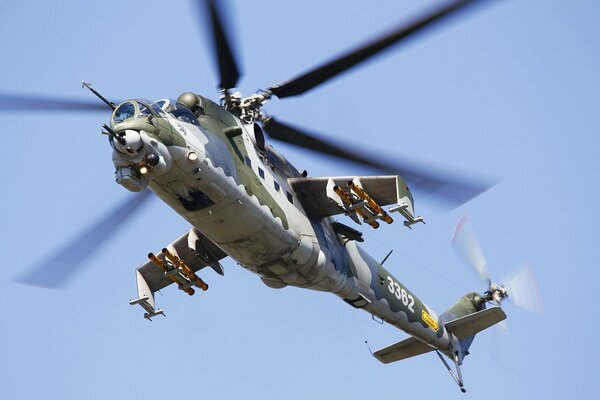 A combat helicopter is flying through the blue sky