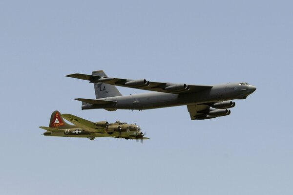 Two planes fly side by side against the gray sky