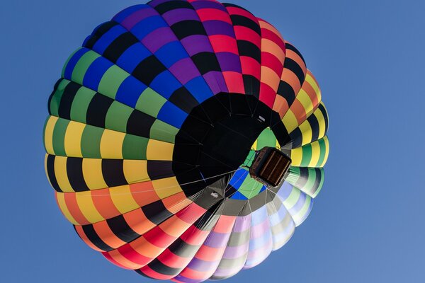 A multicolored balloon with a basket is flying in the sky