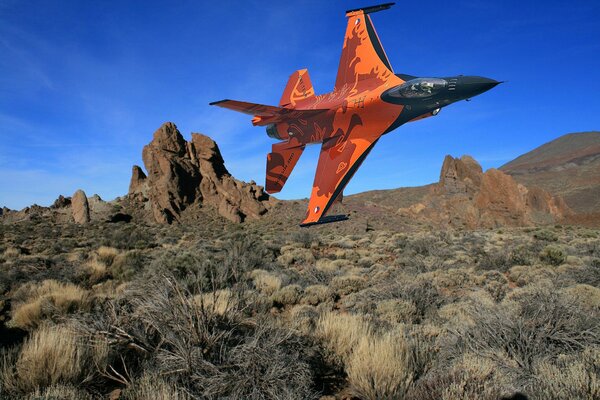 Pomarańczowy myśliwiec nad wzgórzami wchodzi w zakręt