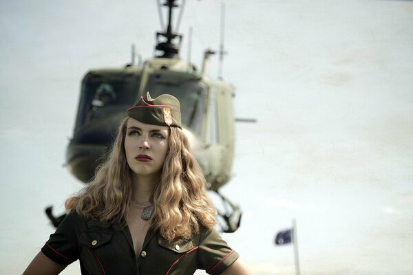 A beautiful girl in a pilot s uniform in front of a helicopter