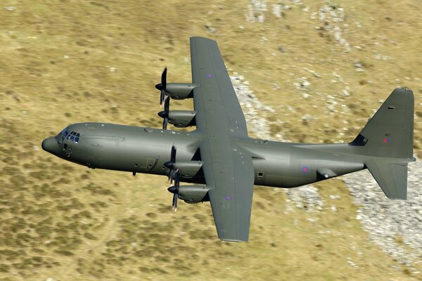 Avion militaire avec quatre hélices vole sur fond de paysage désertique