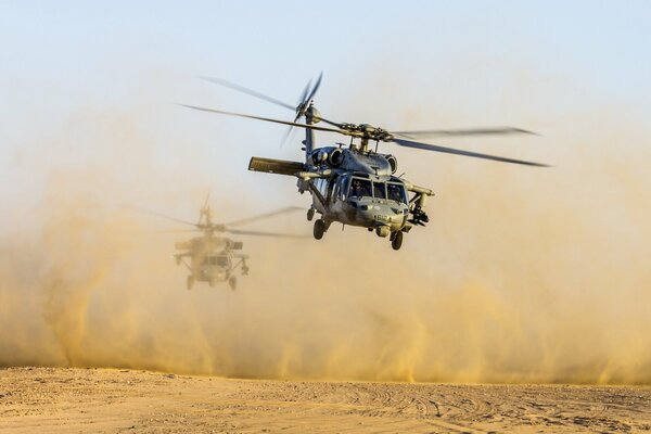Helicopters are flying in the desert raising dust
