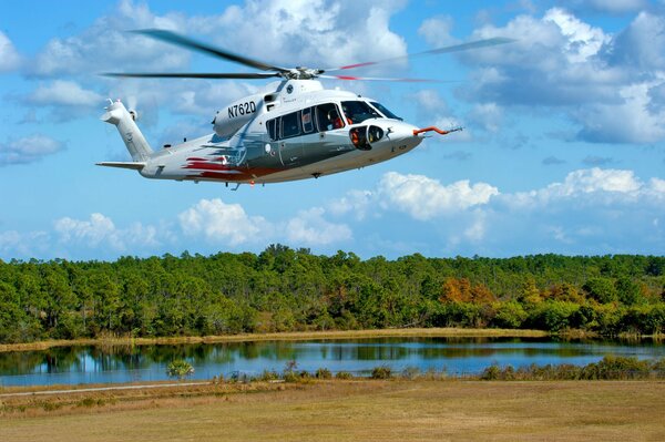 The helicopter is flying against the background of a lake and a forest