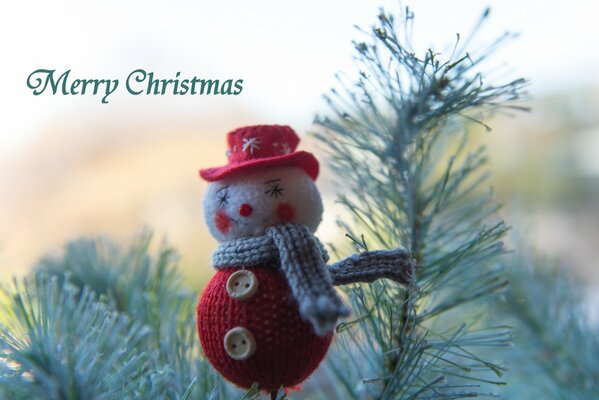 Christmas greetings from a knitted snowman on the background of a fir branch