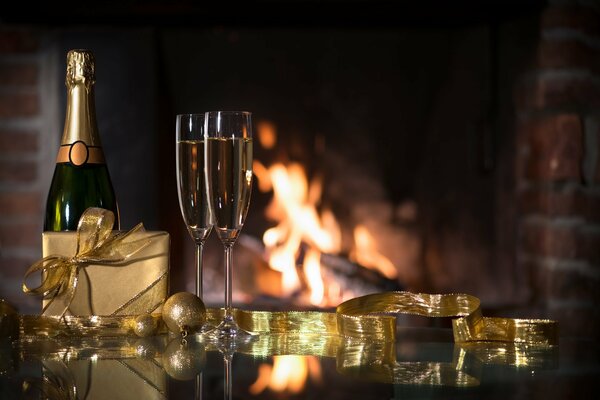 Eine Flasche Champagner, Gläser und ein Geschenk stehen auf dem Tisch. Im Hintergrund brennt ein Kamin