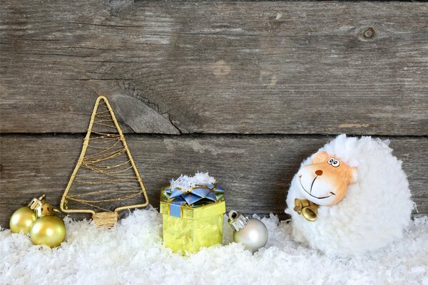 Fluffy goat in the snow with gifts and a Christmas tree