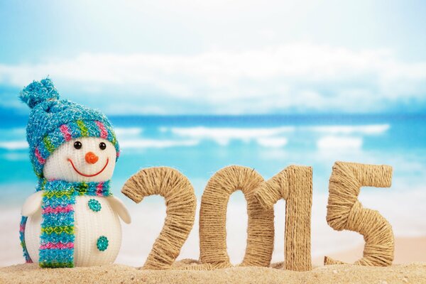 Bonhomme de neige tricoté sur la plage sur fond de mer avec inscription 2015