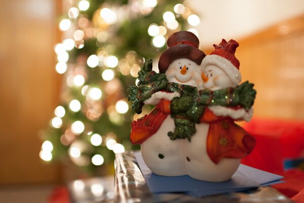 A couple of happy snowmen on the background of a glowing Christmas tree in the distance