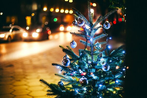 A fir tree with balloons and a garland on the street near the road