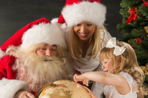 Santa Claus holds a globe that is viewed by a woman and a girl