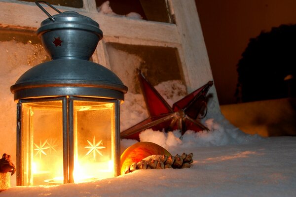Bougie lanterne à la main de Noël dans la neige et les bâtons de cannelle