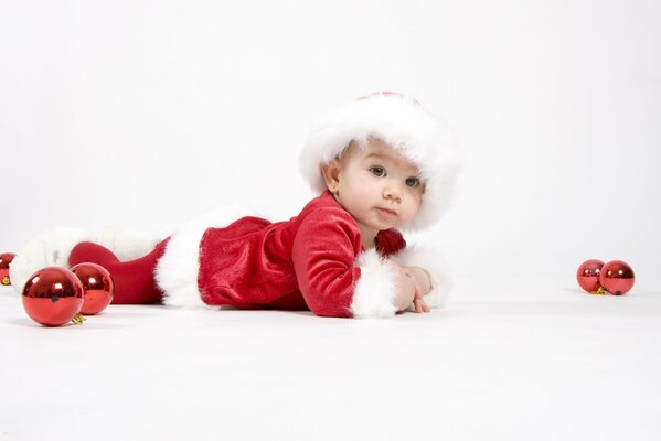 Un niño con un traje de Santa Claus sobre un fondo blanco con juguetes de Navidad rojos