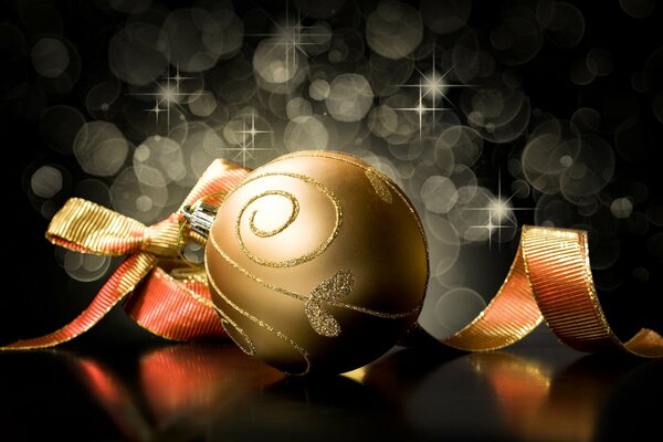 Christmas tree decoration in the form of a golden ball with a ribbon on a black background